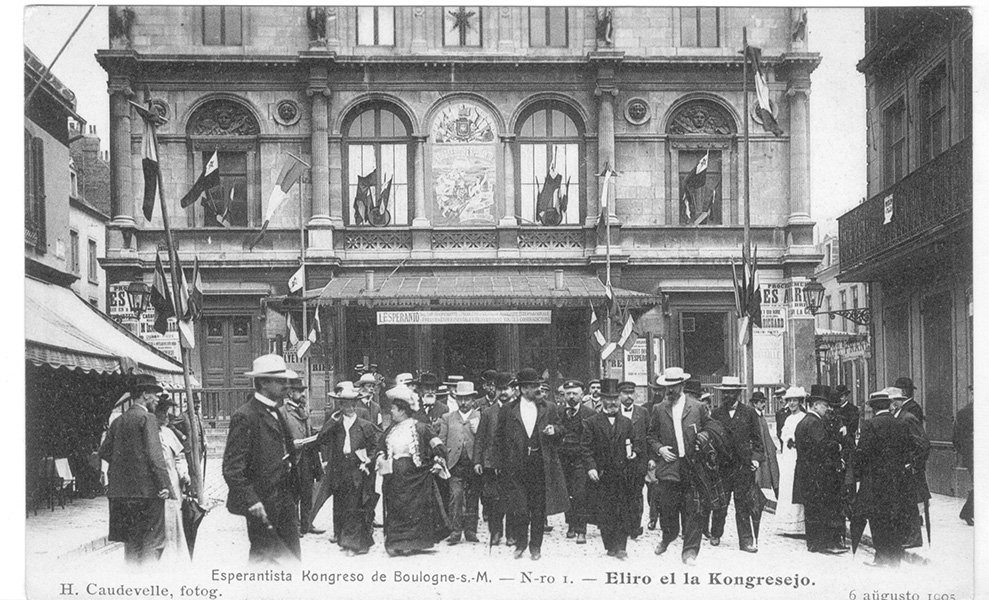 A crowd of well-dressed men and women gather in front of a convention hall in 1905.