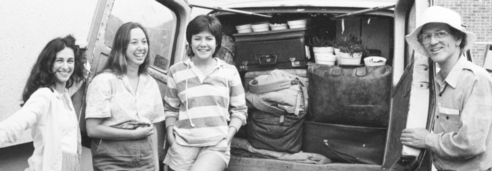 Black and white photograph of four people standing in front of a truck that has its rear doors open, revealing camping supplies inside.