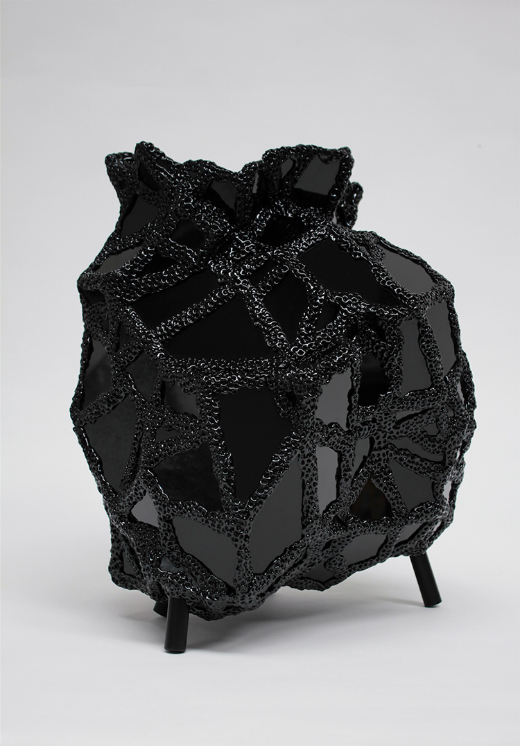 Image shows a black abstract sculpture made up of flat glassy surfaces between a network of textured, black threads.