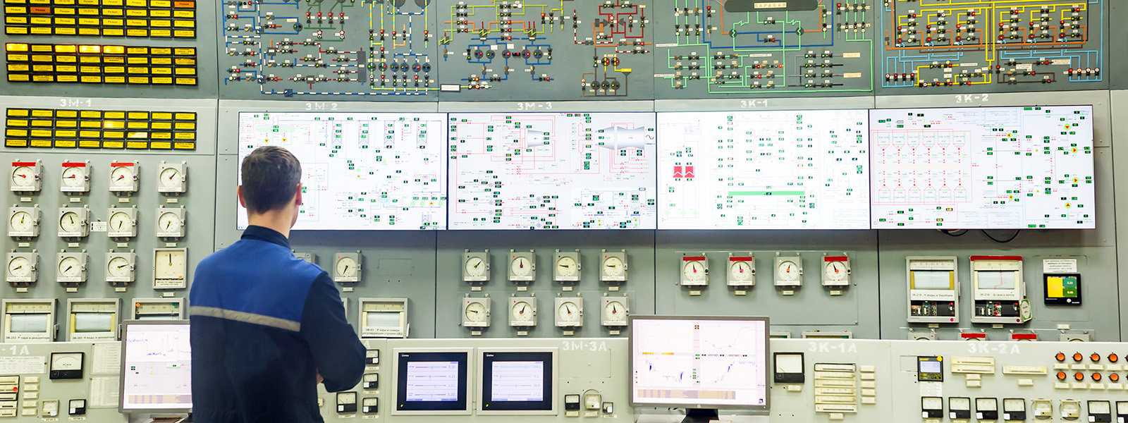 A man gazes at a complicated control panel with switches, indicators and screens.