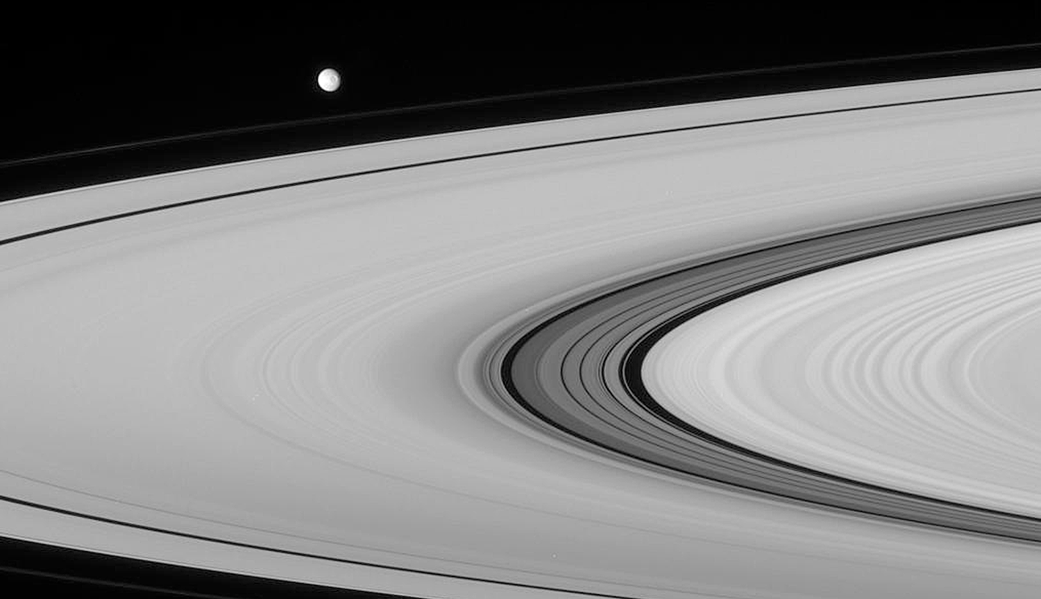 Grayscale image of small orb in the upper left with gray planetary rings taking up much of the rest of the image.