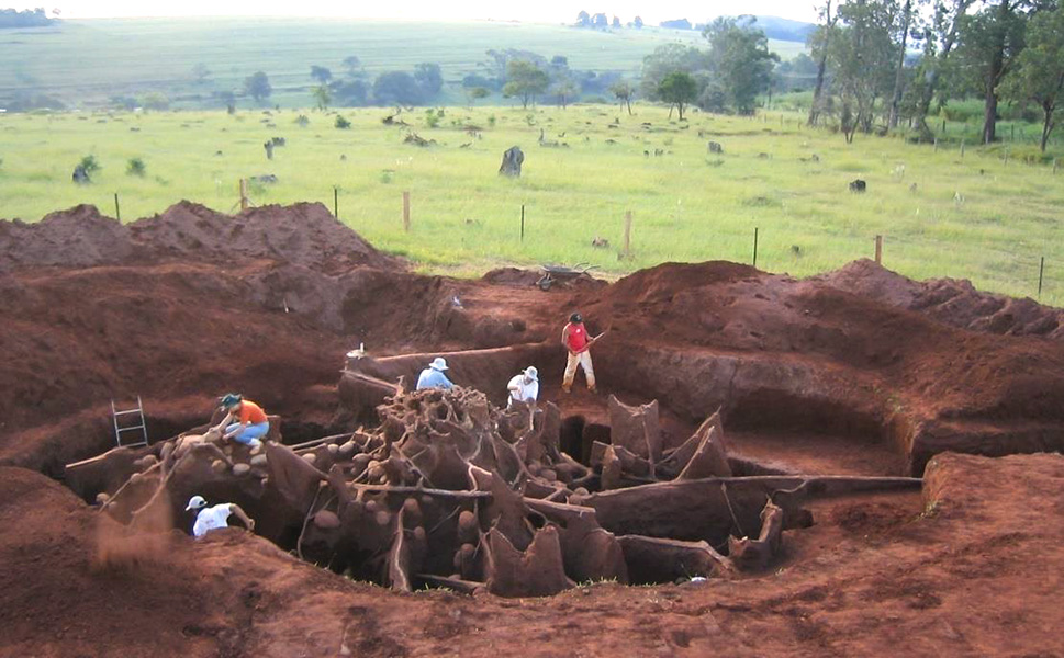 Five people work clearing material from a giant excavated underground structure of tunnels and chambers.