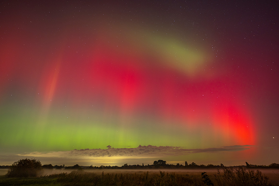 Photo shows a red curtain of color in the evening sky over a field.