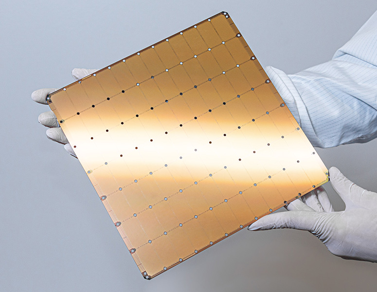 Cerebras chips Gloved hands hold a very large golden chip, the size of a square dinner plate.