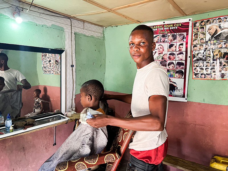 In a small room with a mirror, a man cuts a young child’s hair.