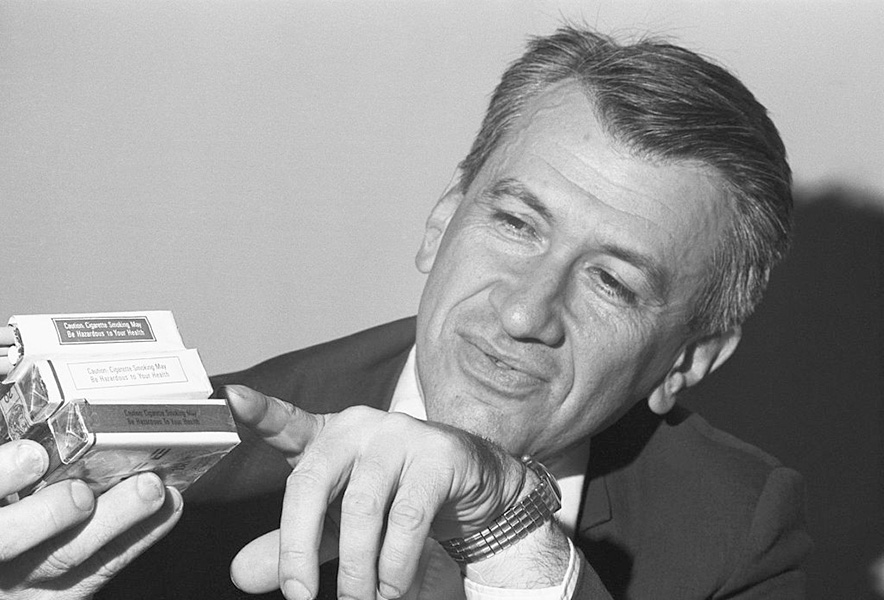 Black-and-white photograph of a man pointing at a warning label on a cigarette pack.