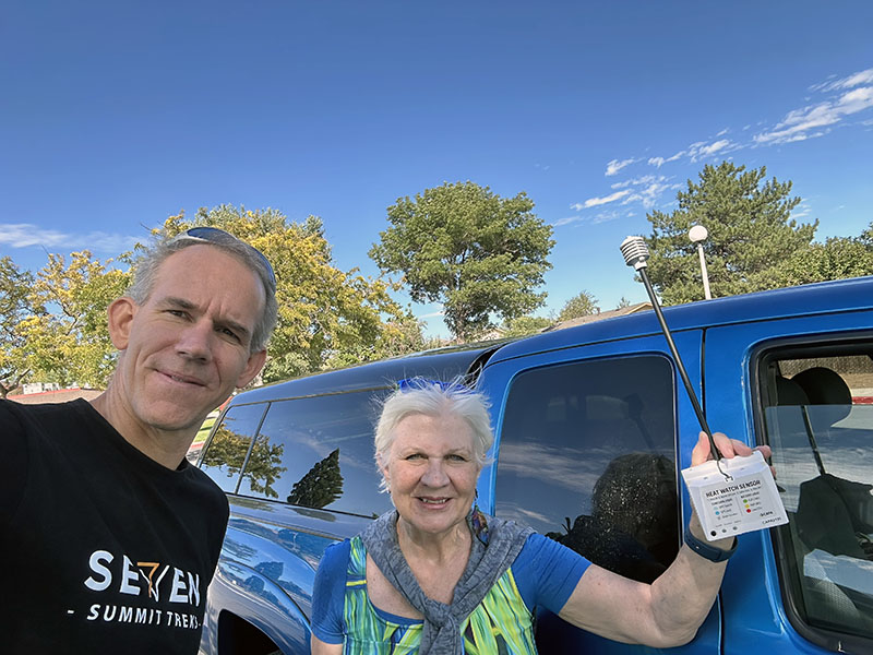 Photo shows a man and a woman in front of a truck holding up a temperature sensor.