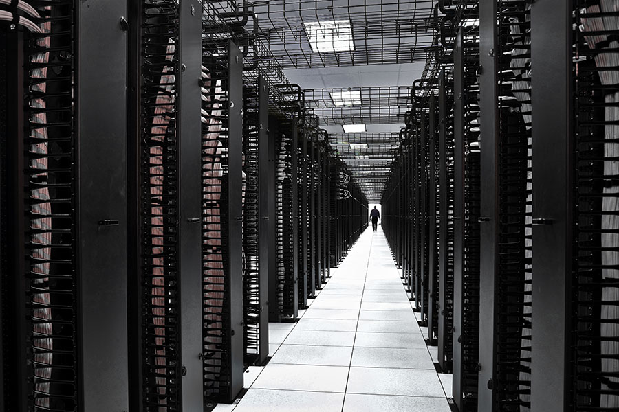 Data center A long hallway between large, dark banks of data center hardware. Someone is walking along the hallway in the distance.