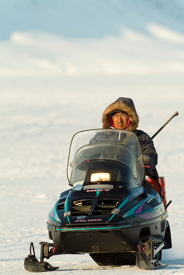 A warmly dressed man rides a snowmobile.