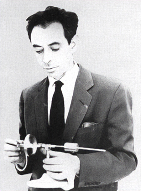 Una foto en blanco y negro muestra a un joven con traje y corbata que mira el instrumento que tiene en la mano.