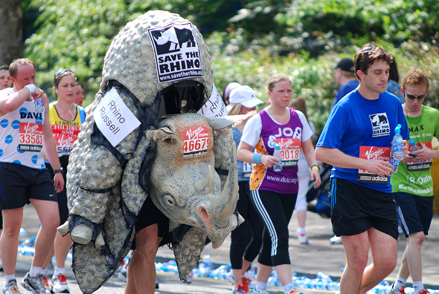 Photo of people in a run, including one person dressed up in a rhino costume. Signs read “Save the rhino.”