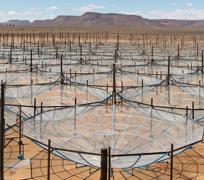 An array of telescopes that look like clear, giant, upside-down umbrellas in the desert against a clear blue sky.