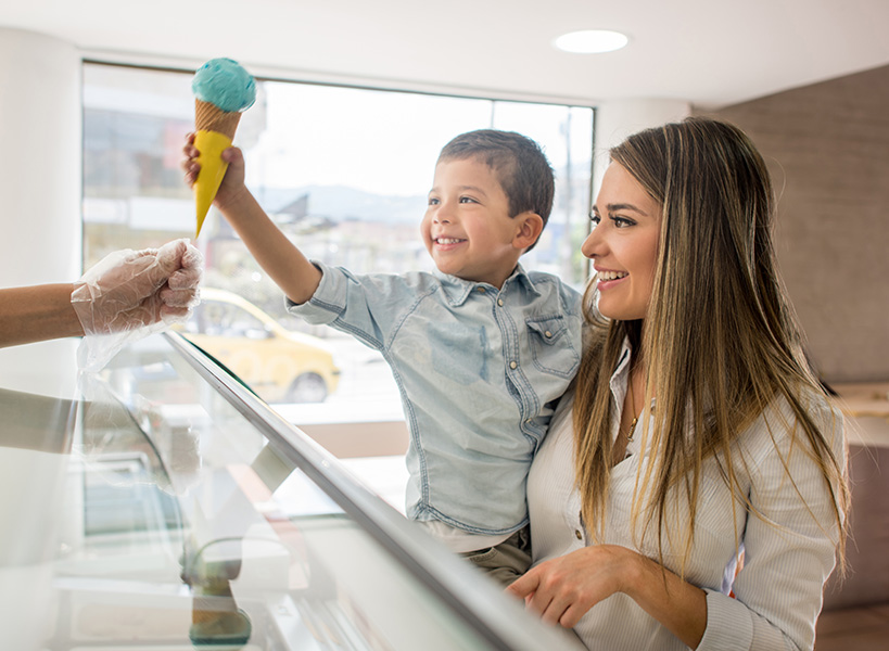 A happy child in his mother’s arms takes an ice cream cone.
