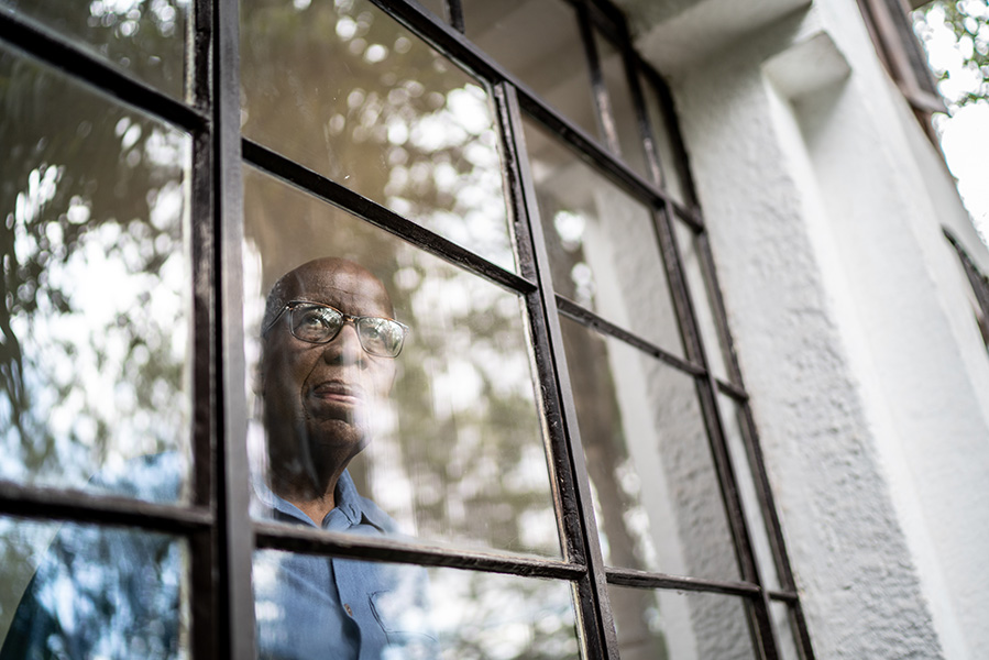 Photo shows an elderly man sadly looking out a window.