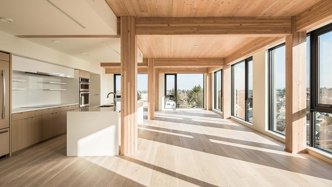 A photo of a modern apartment interior with wooden beams, floor and ceiling. Windows overlook the surrounding neighborhood.