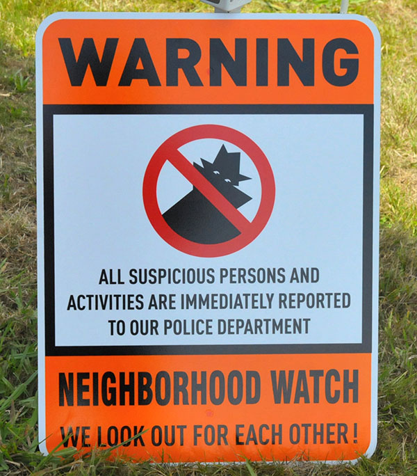 On guard pOrange and white “Neighborhood Watch” sign with a silhouette of a person and warning against suspicious doings.
