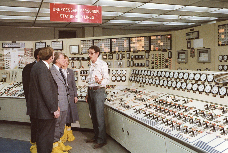 Three Mile Island In a vintage photo, a group of people stand in front of a complex control panel with switches, dials and lights.