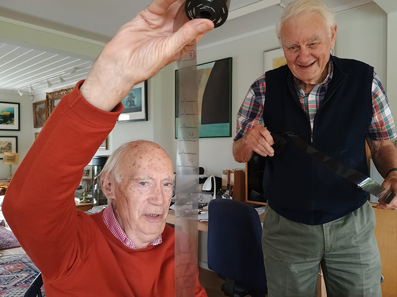 Two men, one in red sweater and one in plaid shirt, examine a film roll.