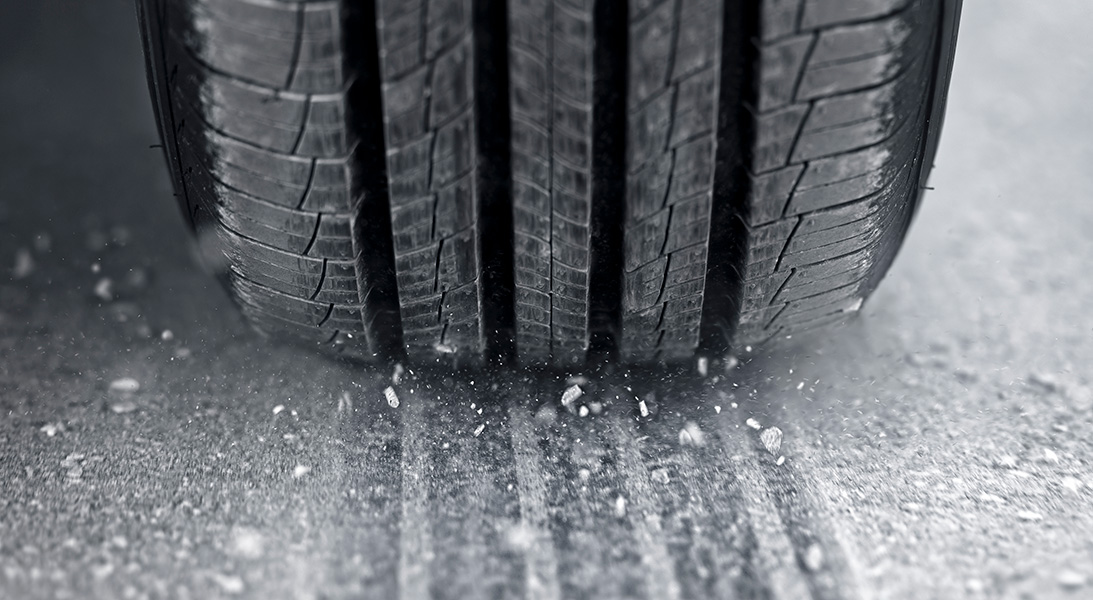 Close-up photograph of a car tire and an asphalt road surface covered with dust and grit.