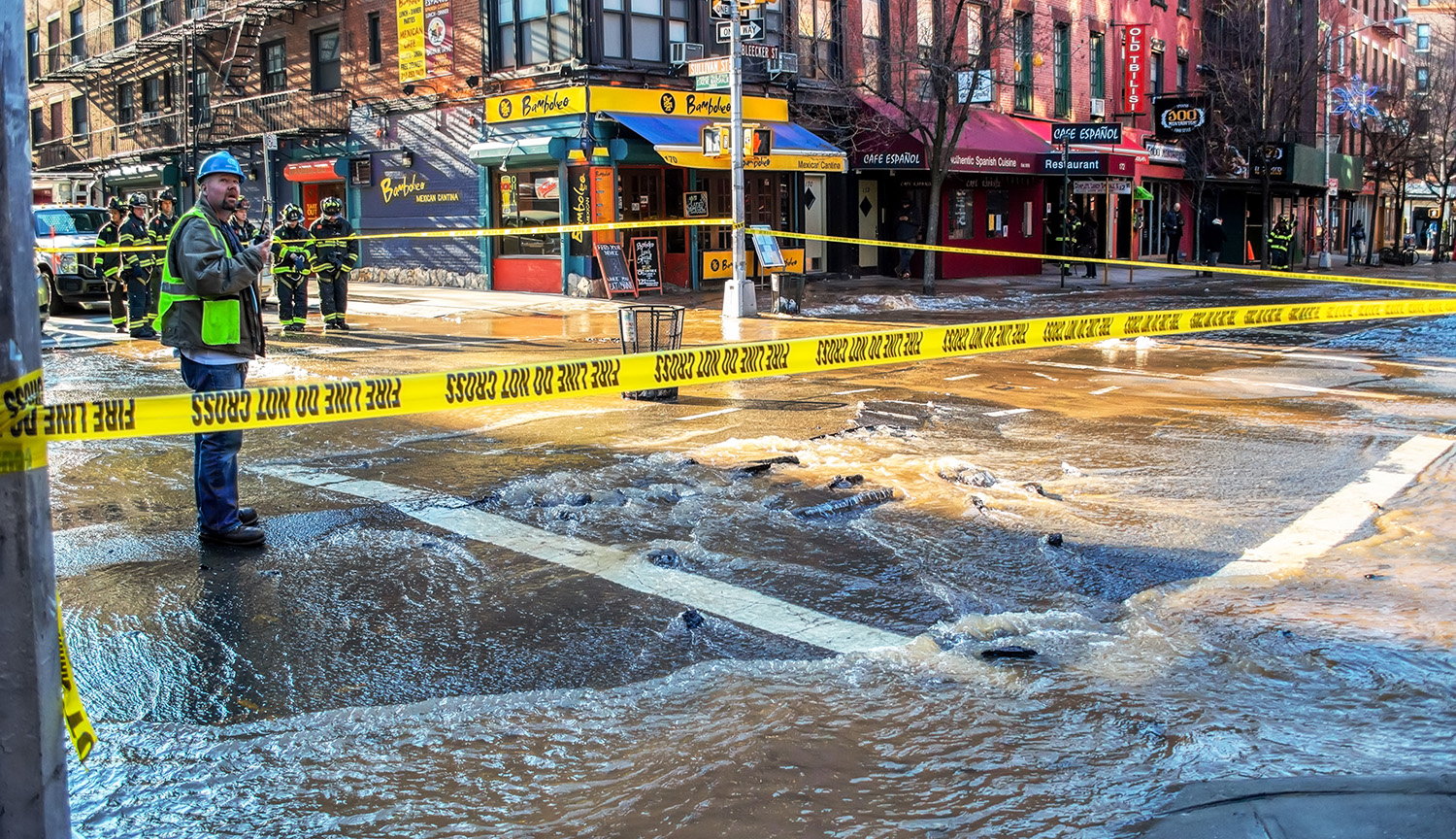 Photo shows a flooded intersection in New York City closed to traffic with yellow caution tape.