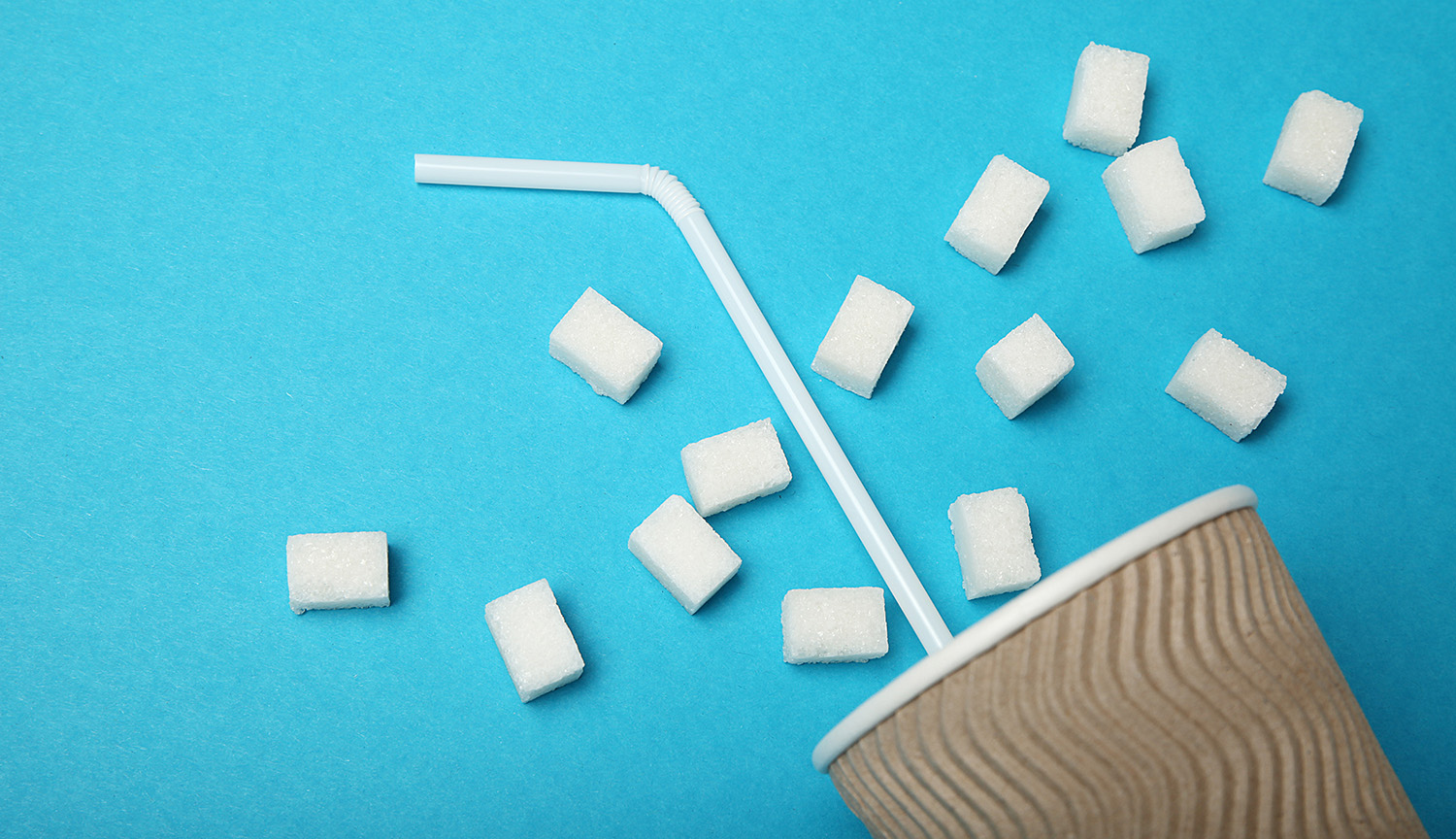 Conceptual art shows a disposable cup, straw and a bunch of sugar lumps on a blue background.